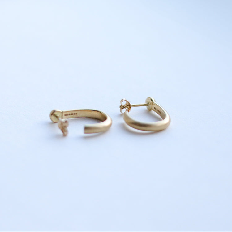 Minimalist 18k yellow gold hoop earrings with a brushed finish, photographed on a white background