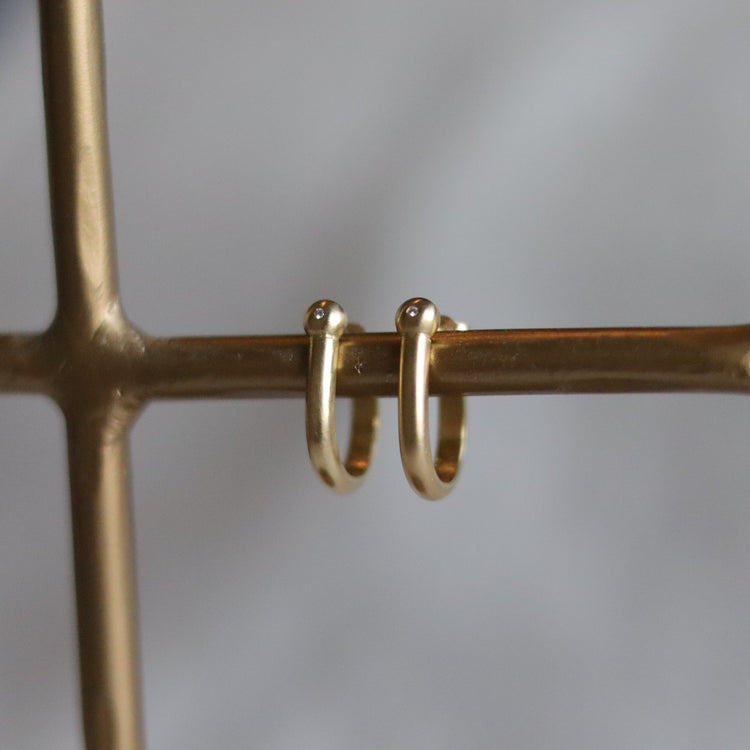 Minimalist 18k yellow gold hoop earrings with a brushed finish, photographed as a matching pair on a stand