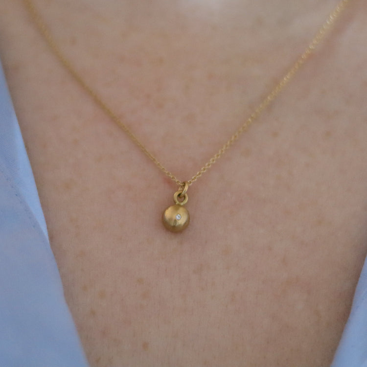Close-up of a 18ct yellow gold pendant necklace worn on the neck, showcasing a minimalist rounded charm diamond set soft light