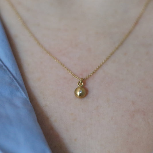 Close-up of a 18ct yellow gold pendant necklace worn on the neck, showcasing a minimalist rounded charm diamond set