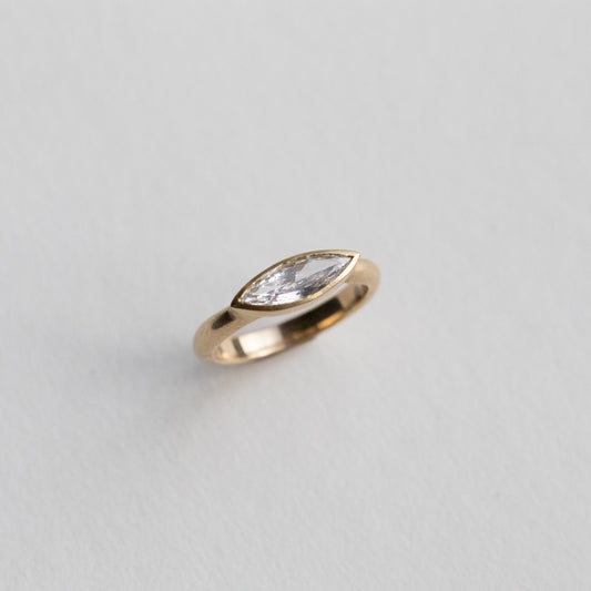 “Elegant 18ct yellow gold ring set with a marquise-cut diamond in a minimalist bezel, paper shot perspective view