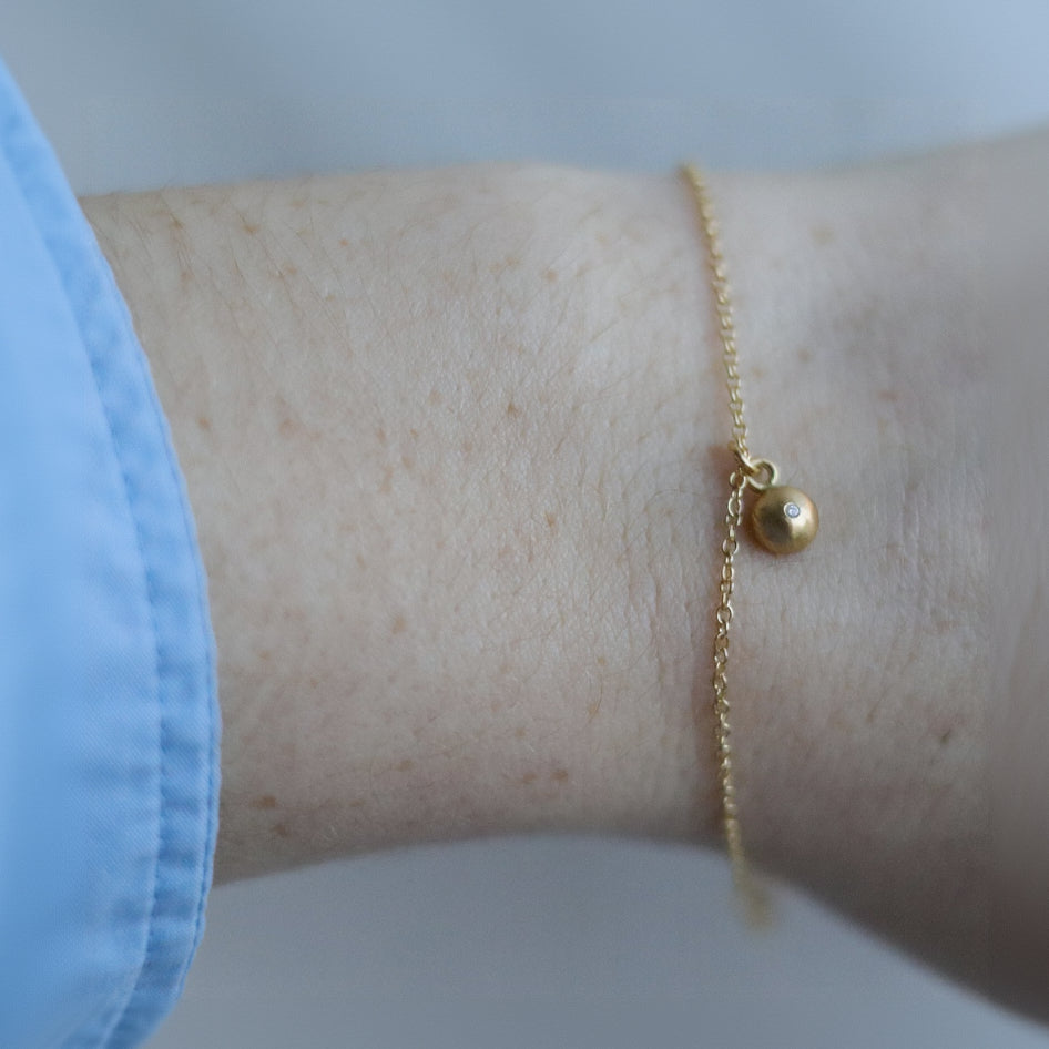goldfinch jewellery Minimalist 18ct yellow gold bracelet featuring a brushed gold spherical pendant set with a diamond on a fine gold chain. pictured on model. 