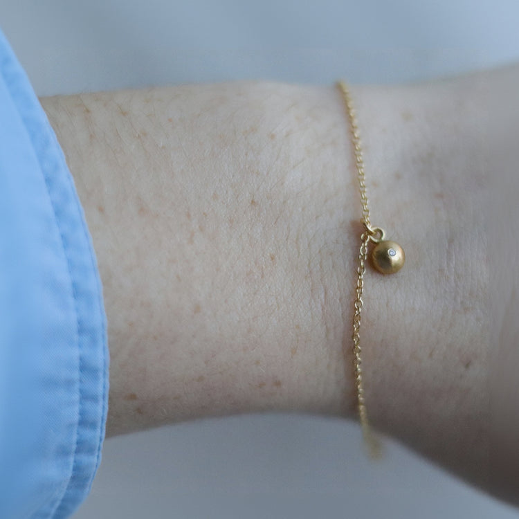 goldfinch jewellery Minimalist 18ct yellow gold bracelet featuring a brushed gold spherical pendant set with a diamond on a fine gold chain. pictured on model. 