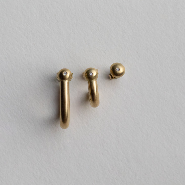 Minimalist 18k diamond set yellow gold hoop and stud earrings with a brushed finish, photographed as a set on paper 