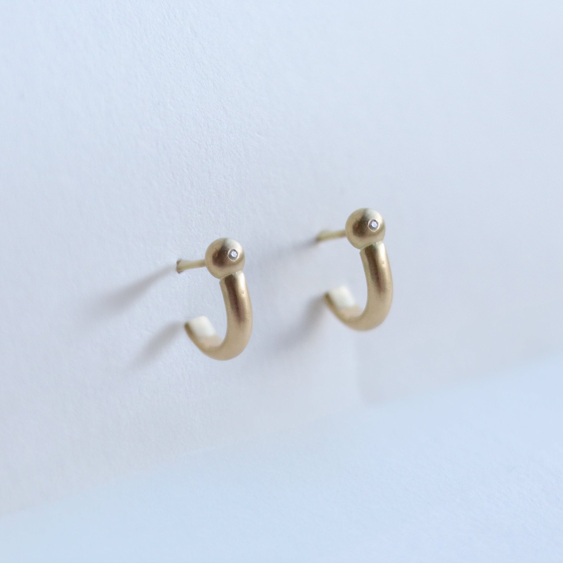 Photo of modern 18ct yellow gold hoop earrings with diamond set rounded ball detail, photographed in soft natural light.
