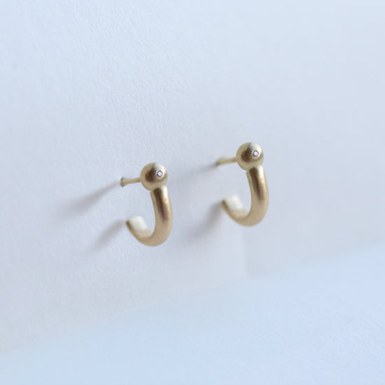 Photo of modern 18ct yellow gold hoop earrings with diamond set rounded ball detail, photographed in soft natural light.