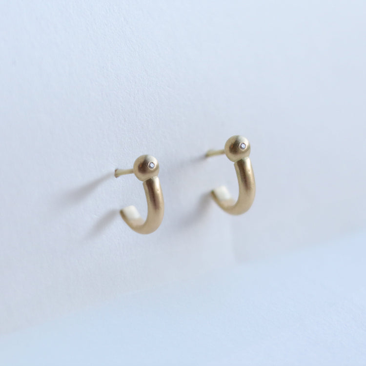 Photo of modern 18ct yellow gold hoop earrings with diamond set rounded ball detail, photographed in soft natural light.