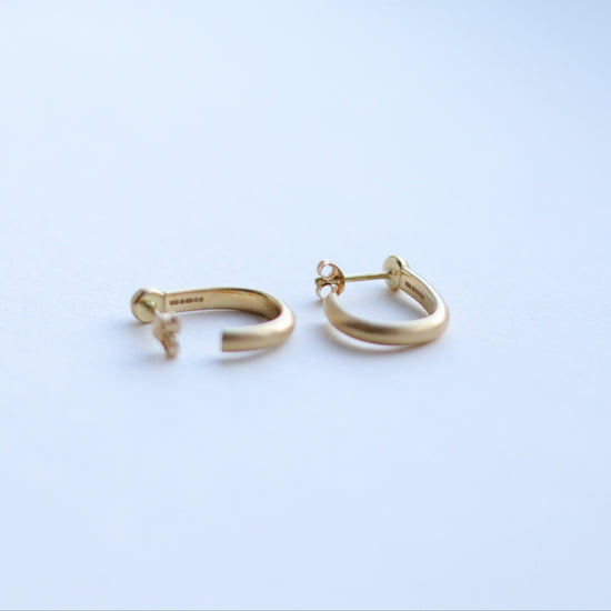 Minimalist 18k yellow gold hoop earrings with a brushed finish, photographed on a white background