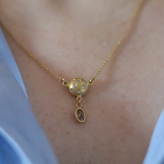 Luxury gold sphere pendant necklace set with diamonds, suspended from a delicate gold chain with brown diamond drop. model shot