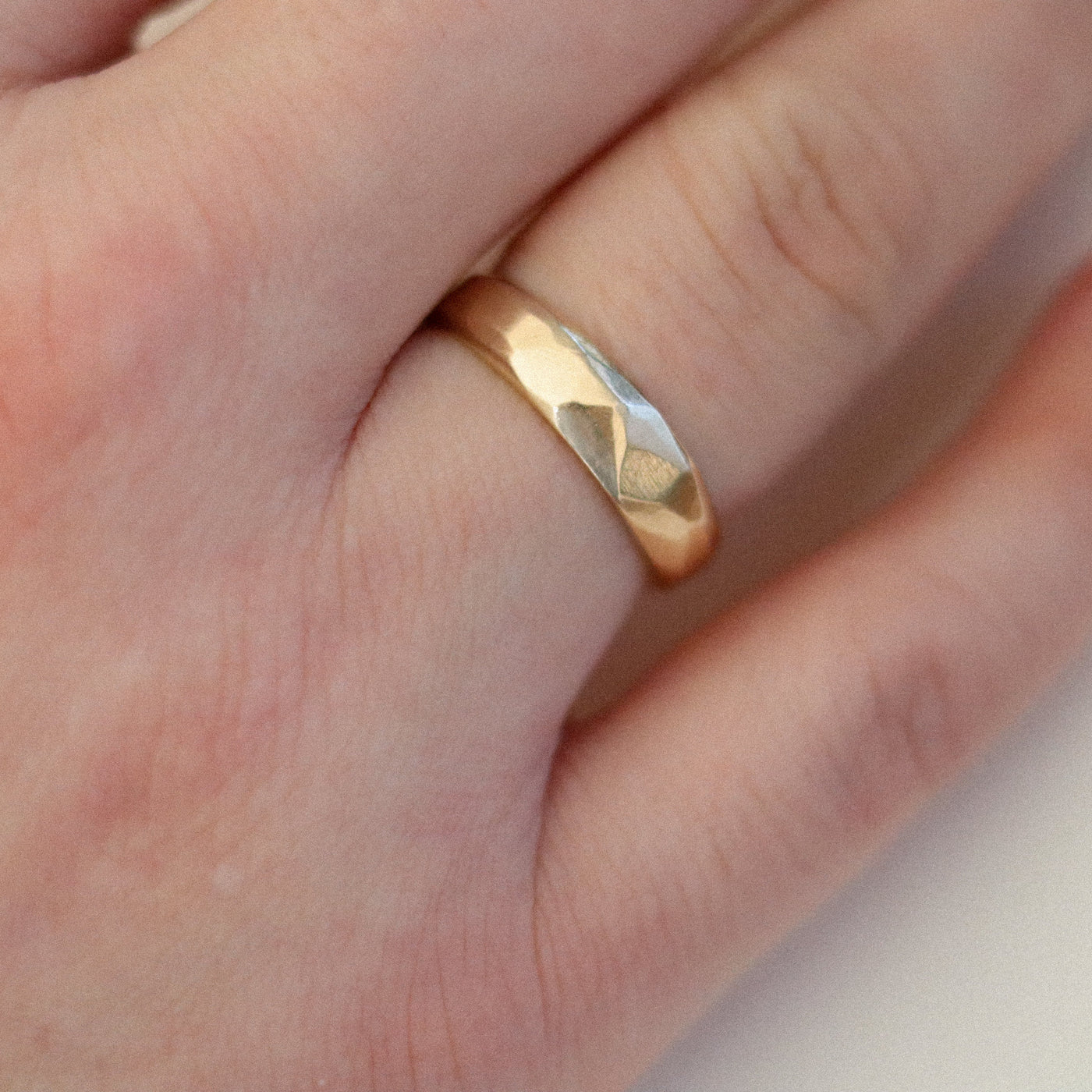 Gold facetted filed ring on a finger with a plain background
