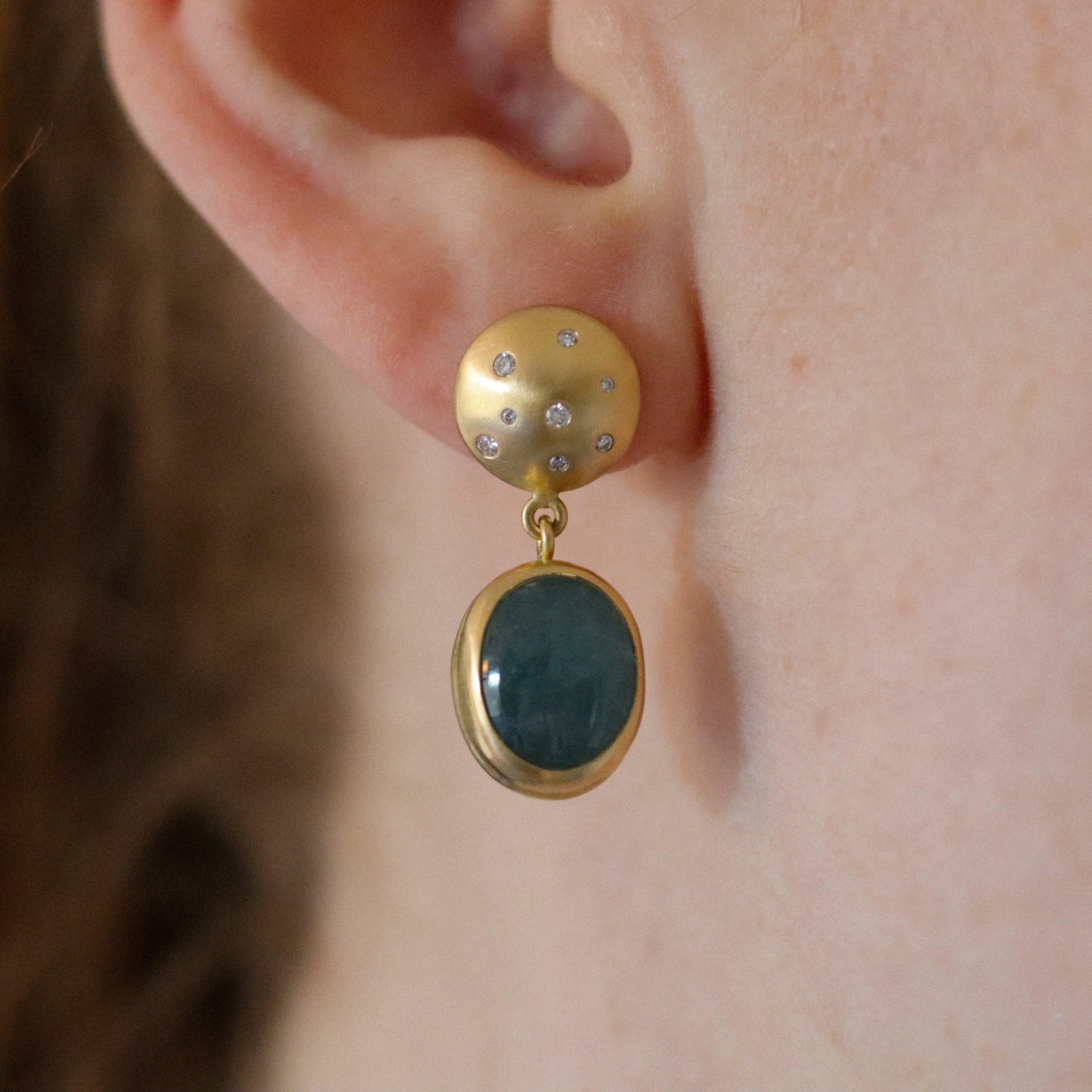 Goldfinch jewellery Statement 18ct yellow gold earrings featuring an oval blue cabochon aquamarine gemstone in a smooth bezel setting, worn on the ear