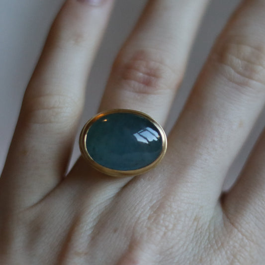 front view of an 18ct yellow gold ring with an oval aquamarine blue cabochon stone worn on the hand