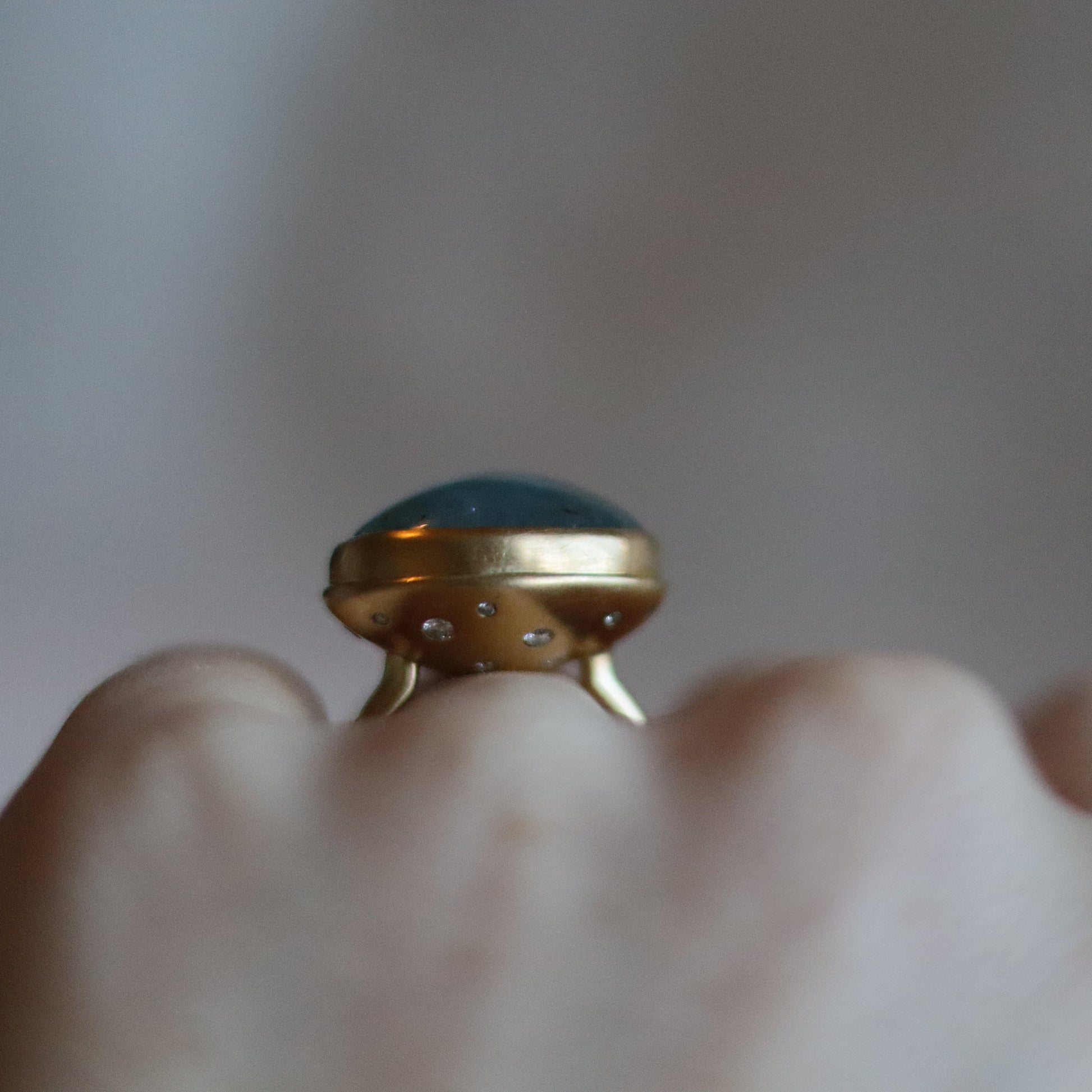 side view of an 18ct yellow gold ring with an oval aquamarine blue cabochon stone, highlighting diamond accents on the band and underneath the setting, photographed on the hand
