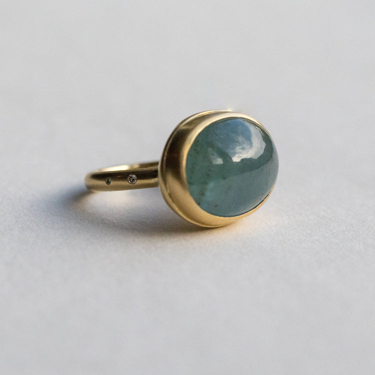 side view of an 18ct yellow gold ring with an oval aquamarine blue cabochon stone, highlighting diamond accents on the band and underneath the setting paper shot