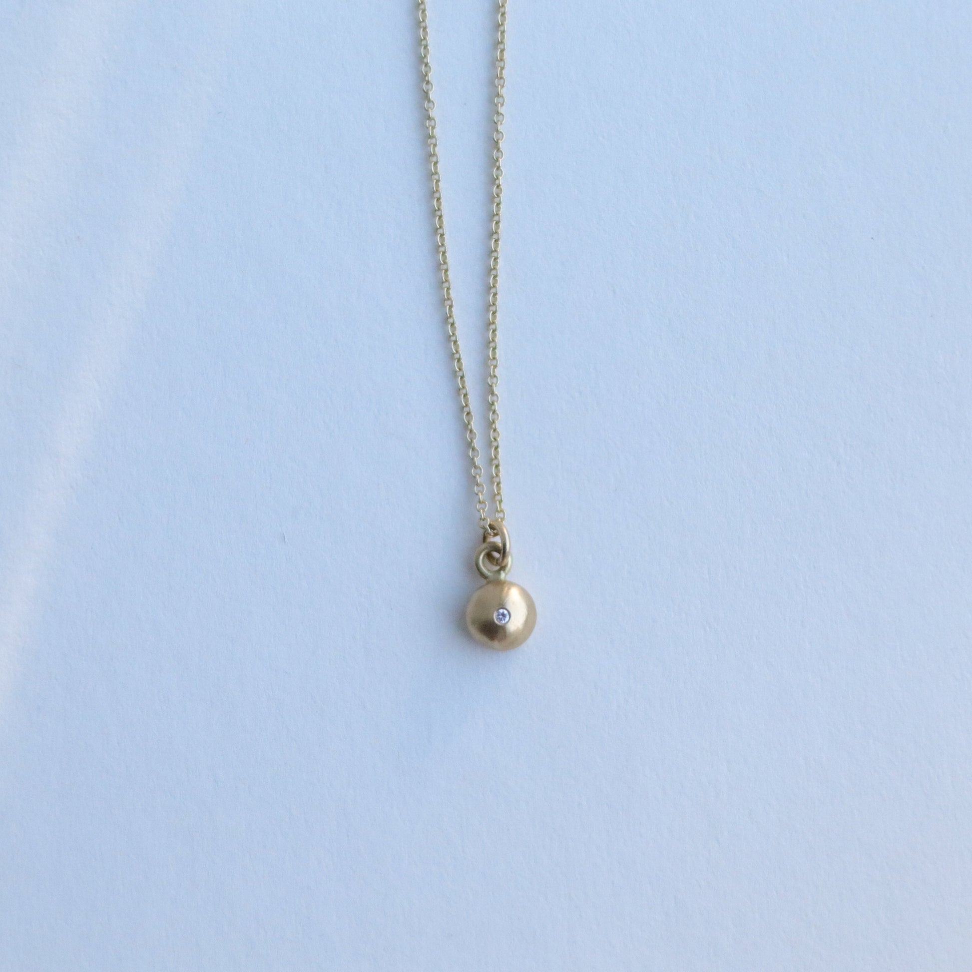 Detail shot of a yellow gold pendant necklace with a softly polished charm suspended from a fine chain 18ct yellow gold diamond set