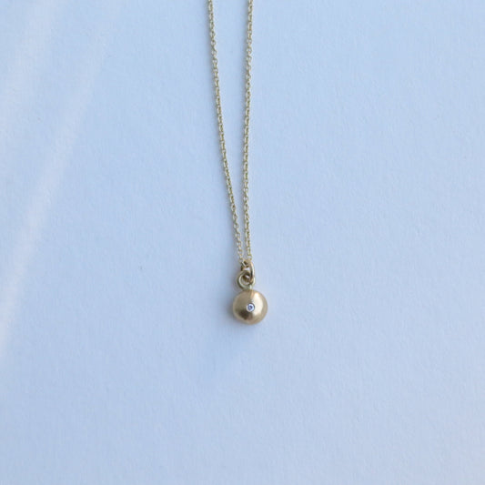 Detail shot of a yellow gold pendant necklace with a softly polished charm suspended from a fine chain 18ct yellow gold diamond set