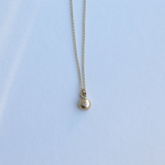 Detail shot of a yellow gold pendant necklace with a softly polished charm suspended from a fine chain 18ct yellow gold diamond set