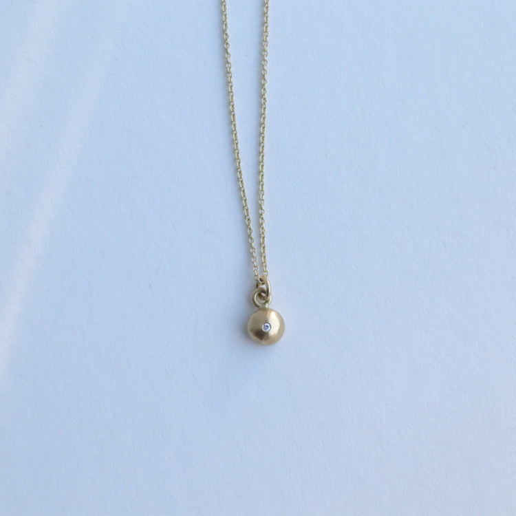 Detail shot of a yellow gold pendant necklace with a softly polished charm suspended from a fine chain 18ct yellow gold diamond set