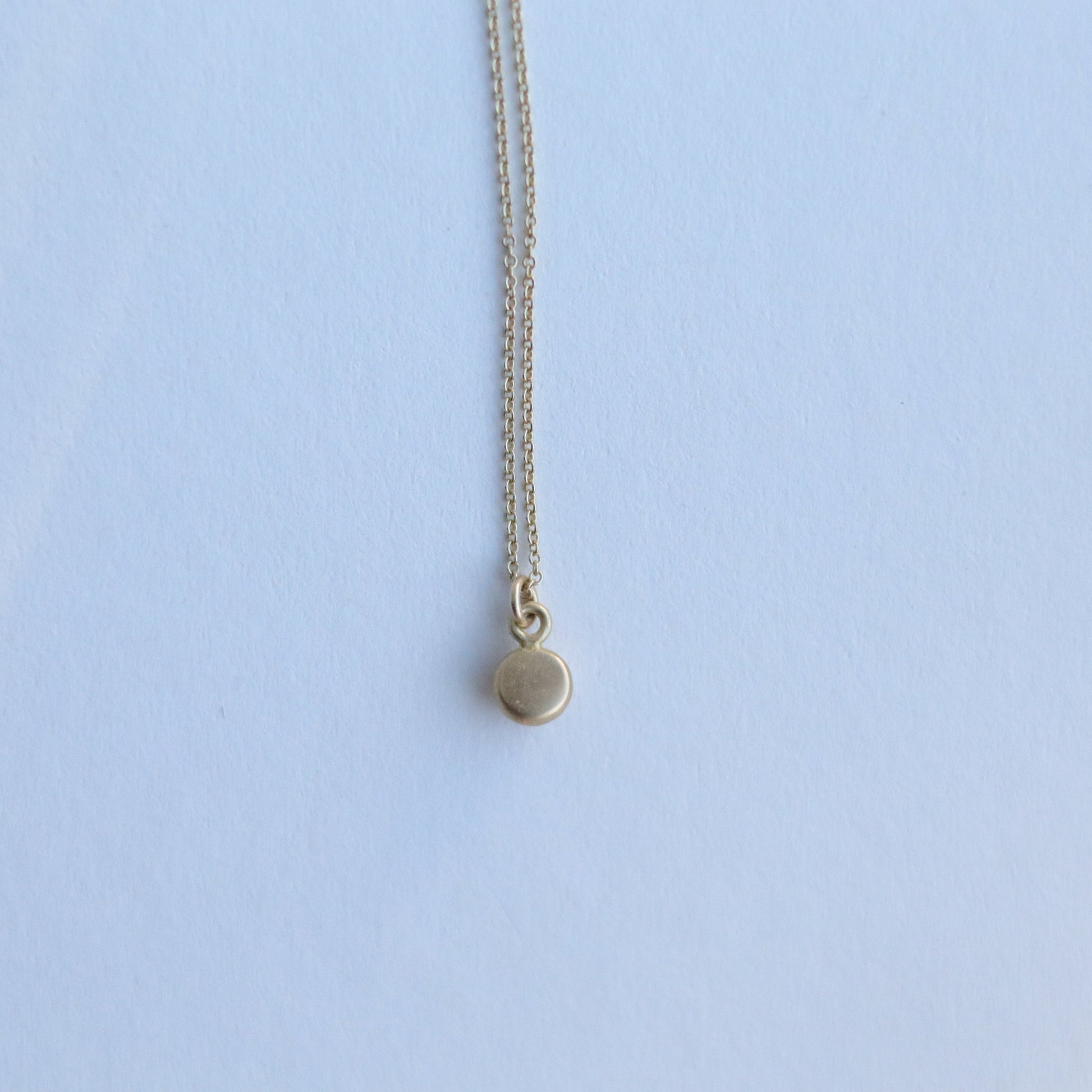 Detail shot of a yellow gold pendant necklace with a softly polished charm suspended from a fine chain 18ct 