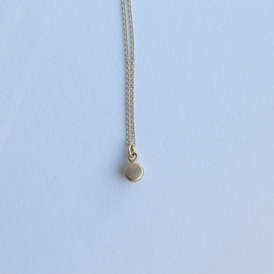 Detail shot of a yellow gold pendant necklace with a softly polished charm suspended from a fine chain 18ct 