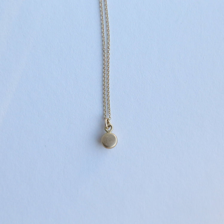 Detail shot of a yellow gold pendant necklace with a softly polished charm suspended from a fine chain 18ct 