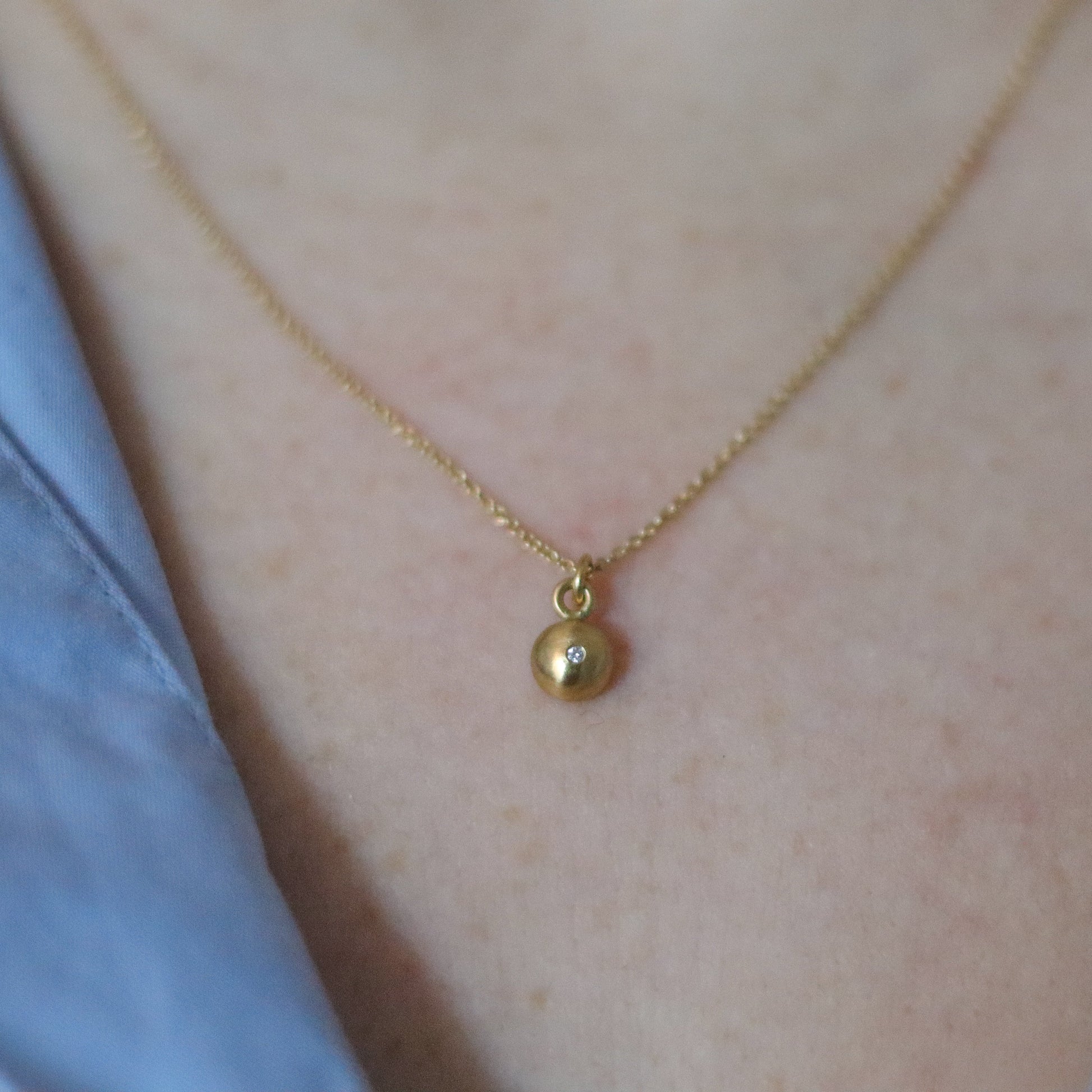 Close-up of a 18ct yellow gold pendant necklace worn on the neck, showcasing a minimalist rounded charm diamond set