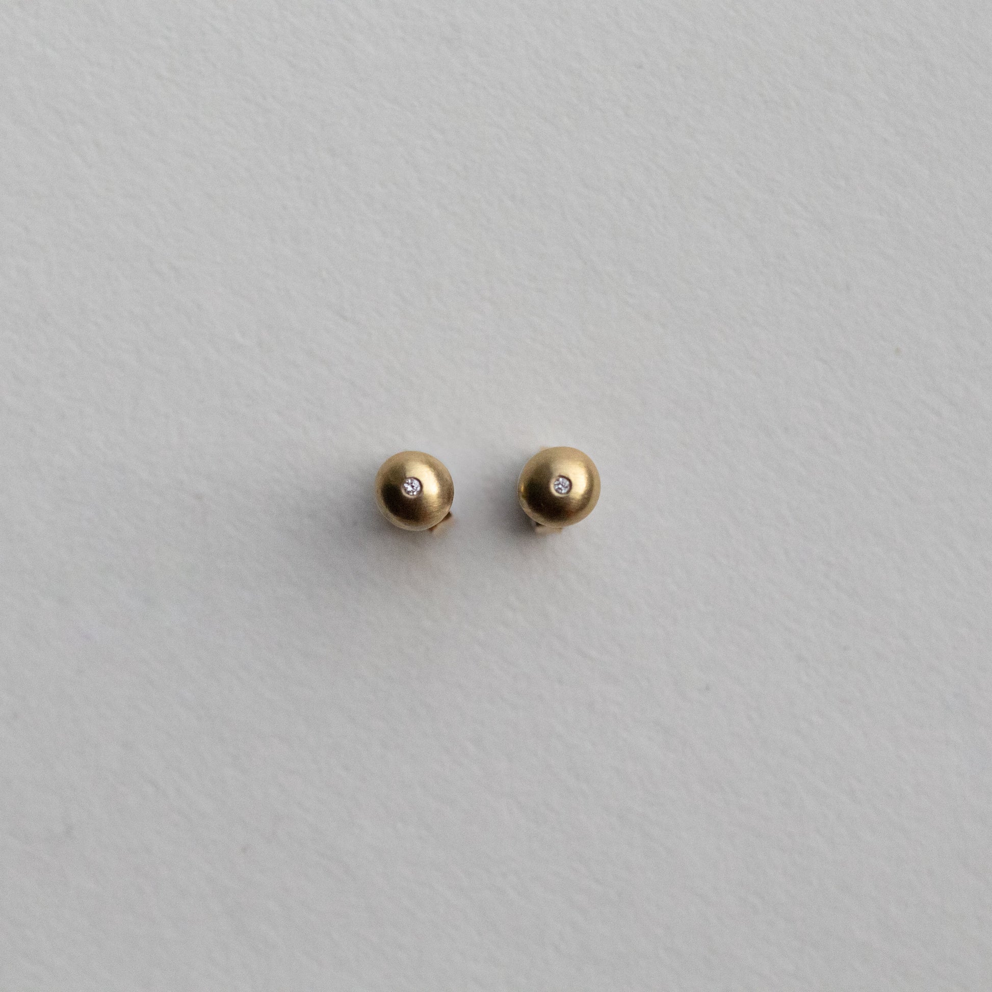 front view of 18ct yellow gold stud earrings highlighting the curved silhouette and satin surface with diamonds