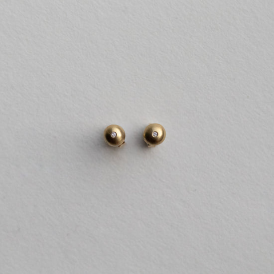 front view of 18ct yellow gold stud earrings highlighting the curved silhouette and satin surface with diamonds