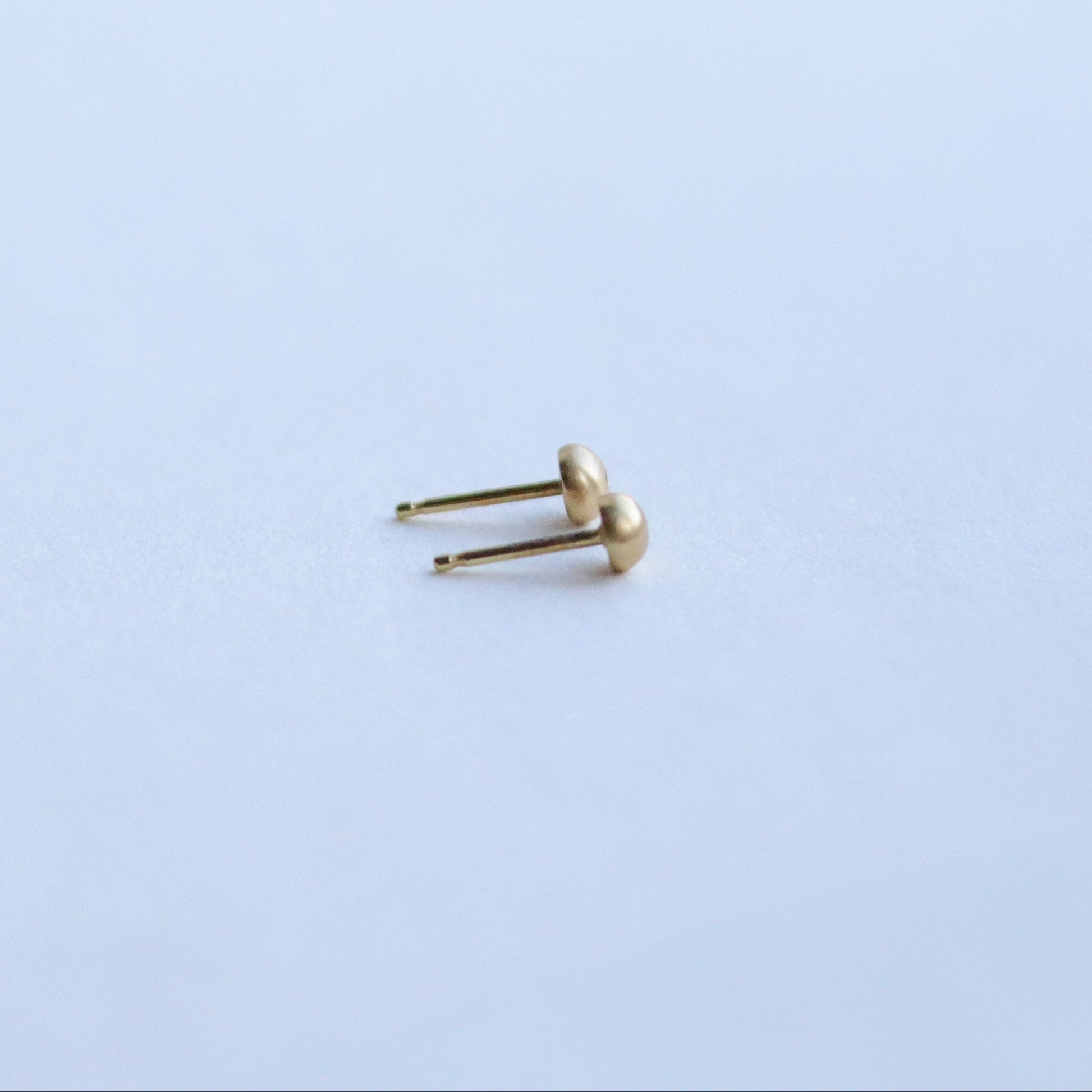 Side view of 18ct yellow gold stud earrings highlighting the curved silhouette and satin surface with diamonds