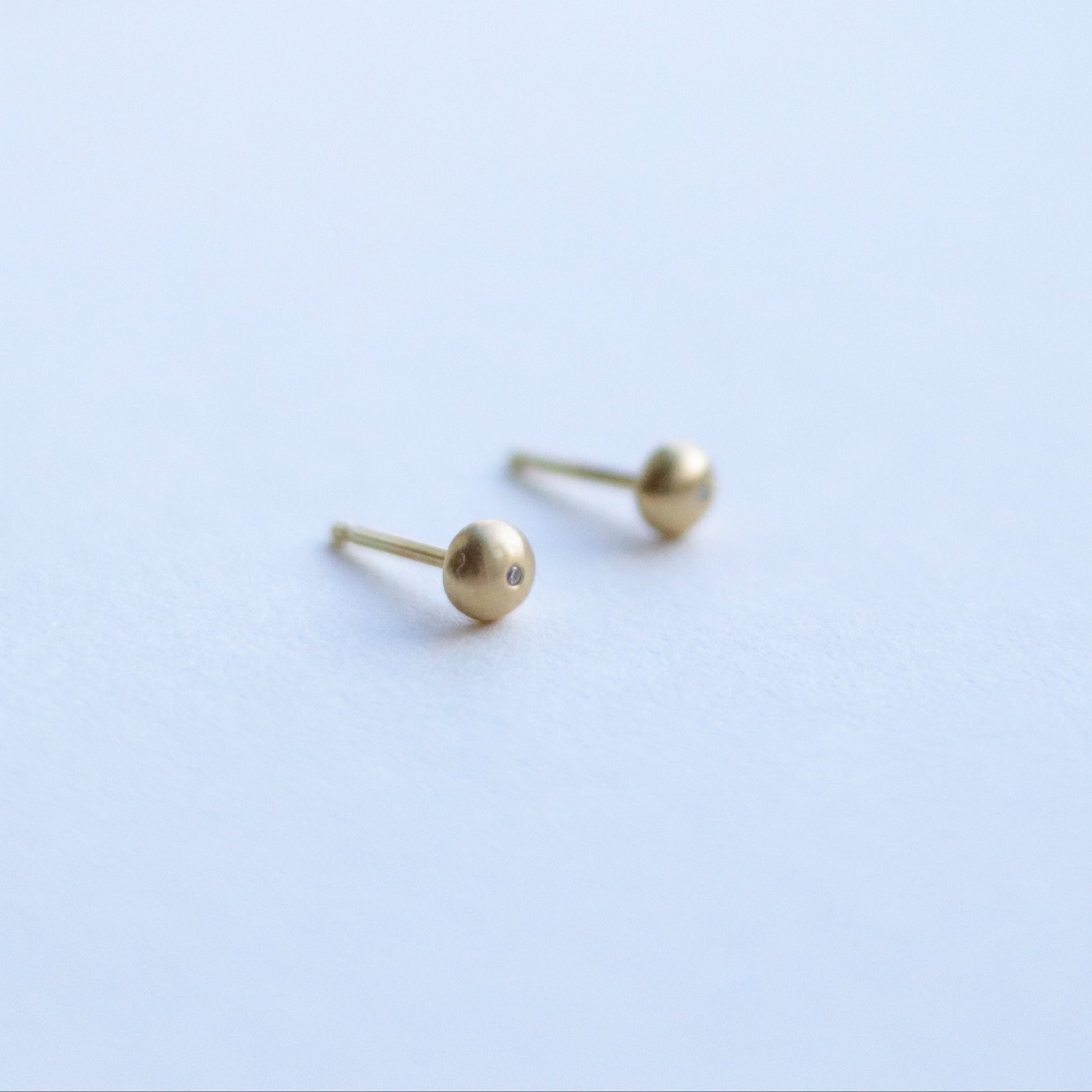 angled view of 18ct yellow gold stud earrings highlighting the curved silhouette and satin surface with diamonds