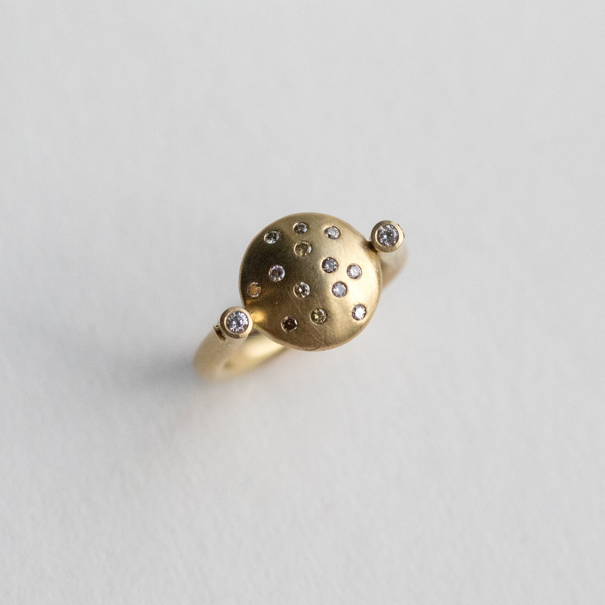 Modern 18ct yellow gold ring with a matte circular spinning disc speckle set with a central natural brown cognac diamonds and white side diamonds, paper shot at angle underside