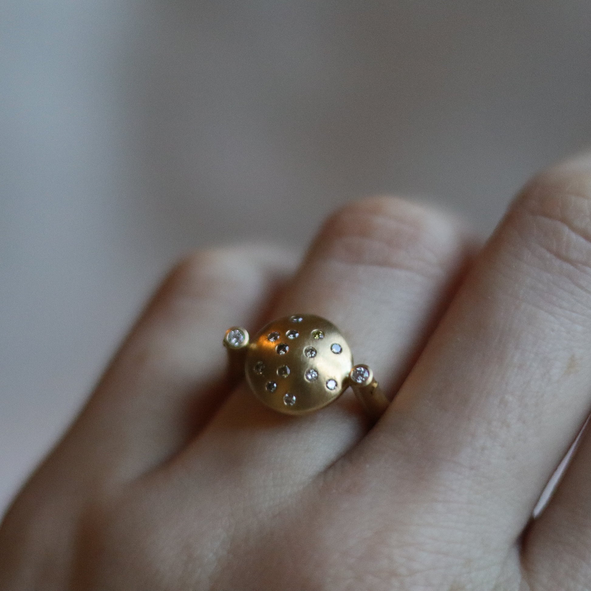 Modern 18ct yellow gold ring with a matte circular spinning disc speckle set with a central natural brown cognac diamonds and white side diamonds, worn on the hand at angle