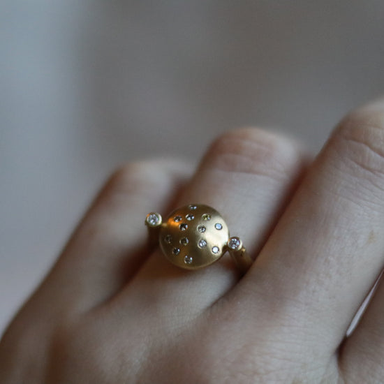 Modern 18ct yellow gold ring with a matte circular spinning disc speckle set with a central natural brown cognac diamonds and white side diamonds, worn on the hand at angle