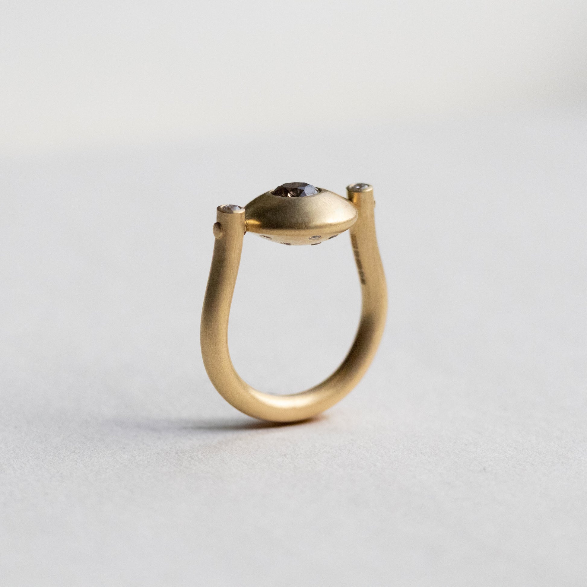 Modern 18ct yellow gold ring with a matte circular spinning disc speckle set with a central natural brown cognac diamond and white side diamonds, paper shot side view