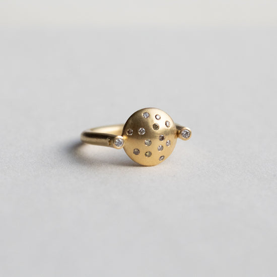 Modern 18ct yellow gold ring with a matte circular spinning disc speckle set with a central natural brown cognac diamonds and white side diamonds, paper shot at angle with underneath