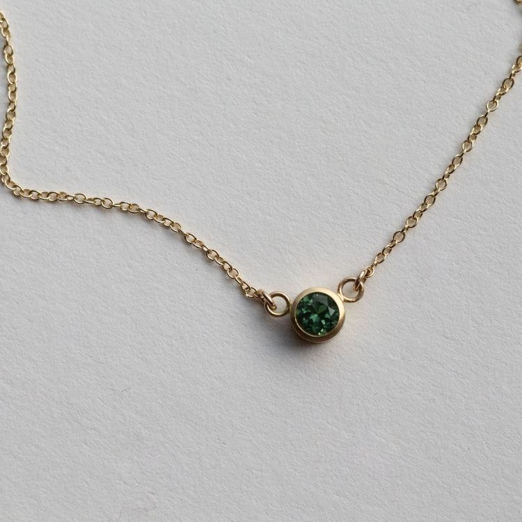 Minimalist brushed 18ct yellow gold bracelet featuring a mint green tourmaline on a fine gold chain on paper