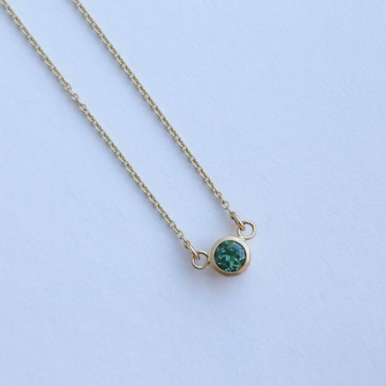 Minimalist brushed 18ct yellow gold necklace featuring a mint green tourmaline on a fine gold chain on paper