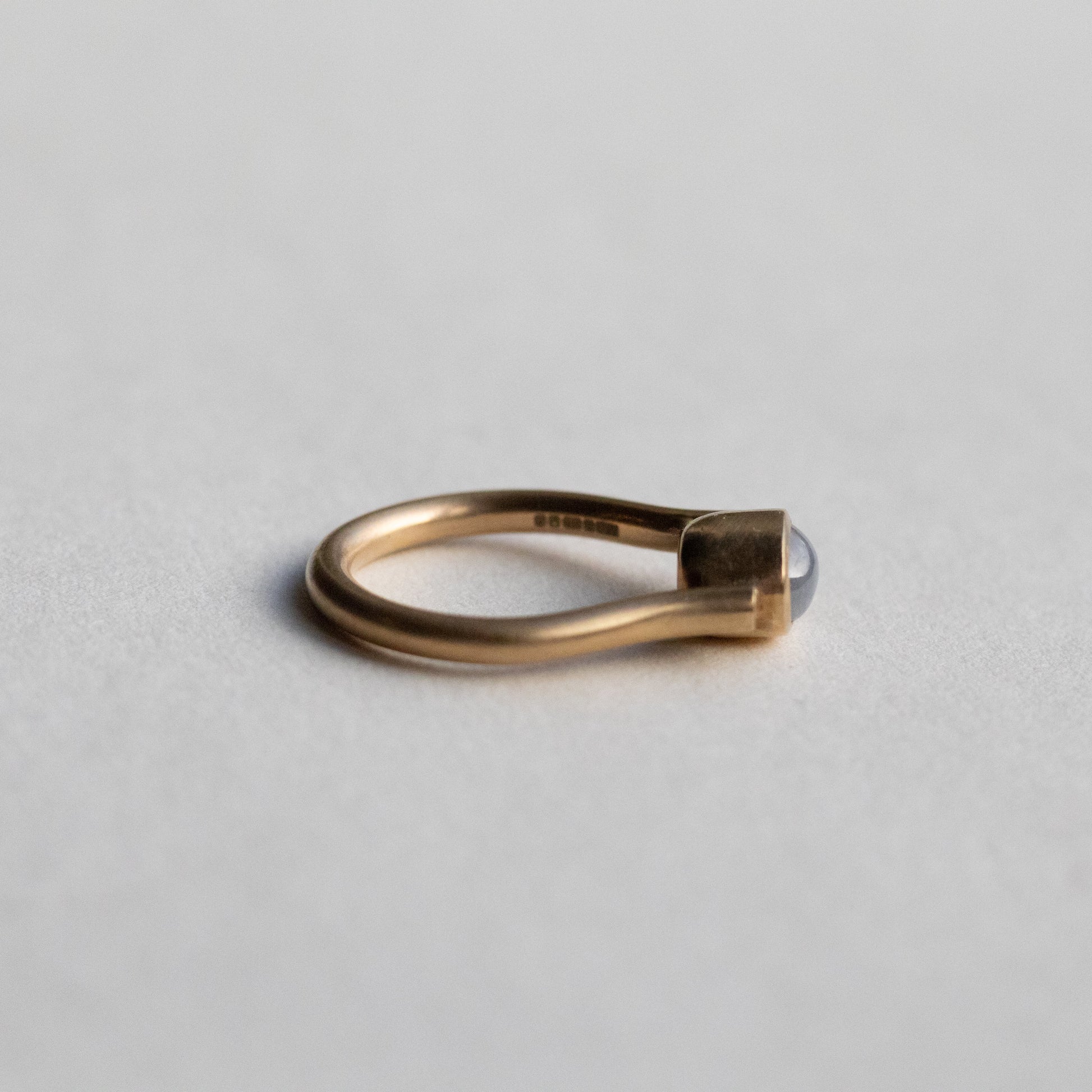Modern 9ct yellow gold pillar ring with a single bezel-set grey cabochon star sapphire, photographed as flat side view