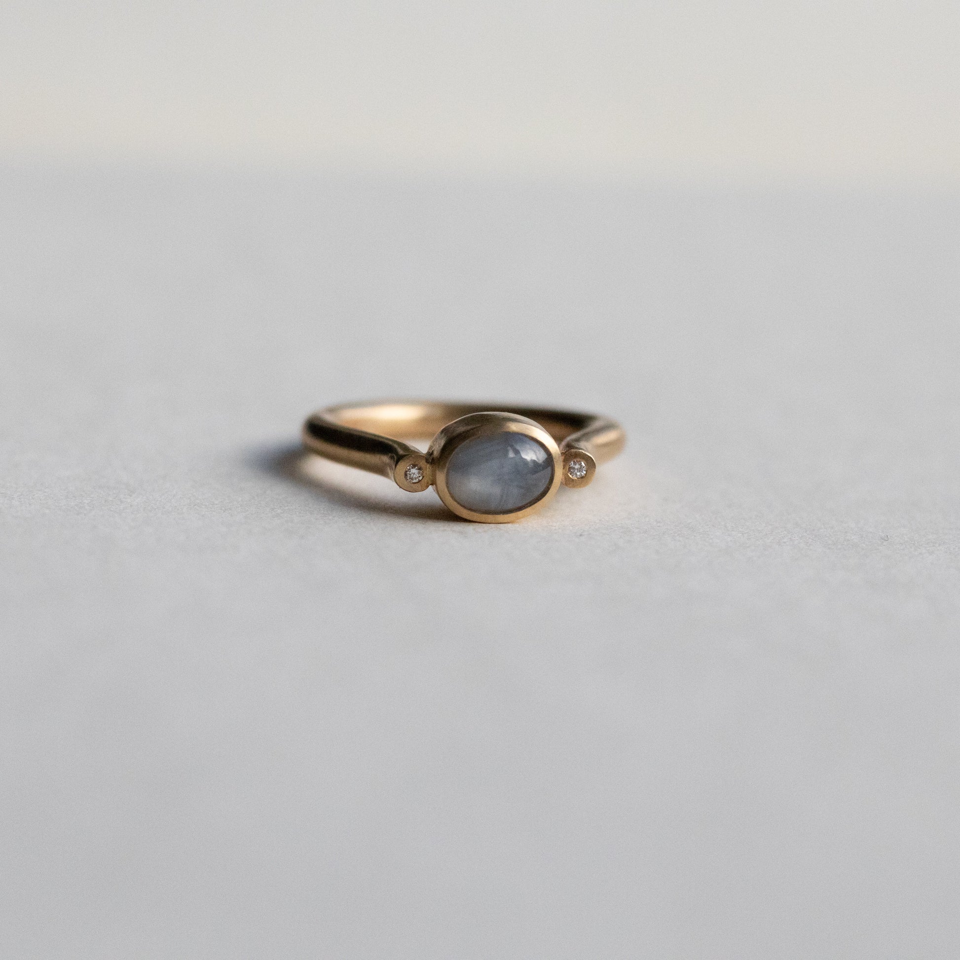 Modern 9ct yellow gold pillar ring with a single bezel-set grey cabochon star sapphire, photographed from a front view