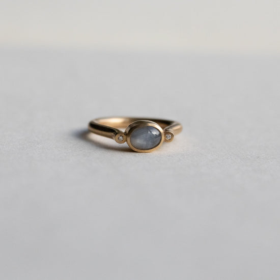 Modern 9ct yellow gold pillar ring with a single bezel-set grey cabochon star sapphire, photographed from a front view