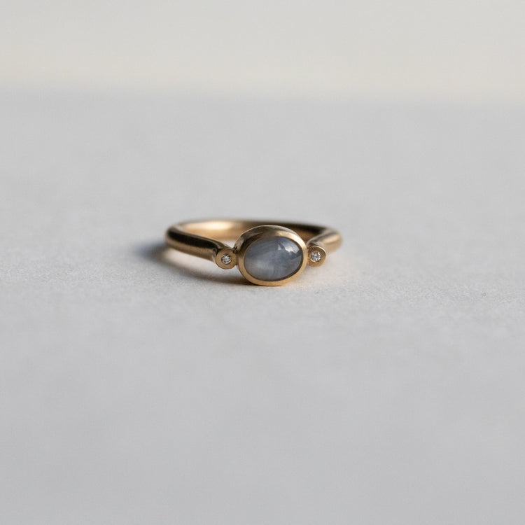 Modern 9ct yellow gold pillar ring with a single bezel-set grey cabochon star sapphire, photographed from a front view