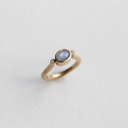 goldfinch jewellery Modern 9ct yellow gold pillar ring with a single bezel-set grey cabochon star sapphire, photographed from an angled perspective.