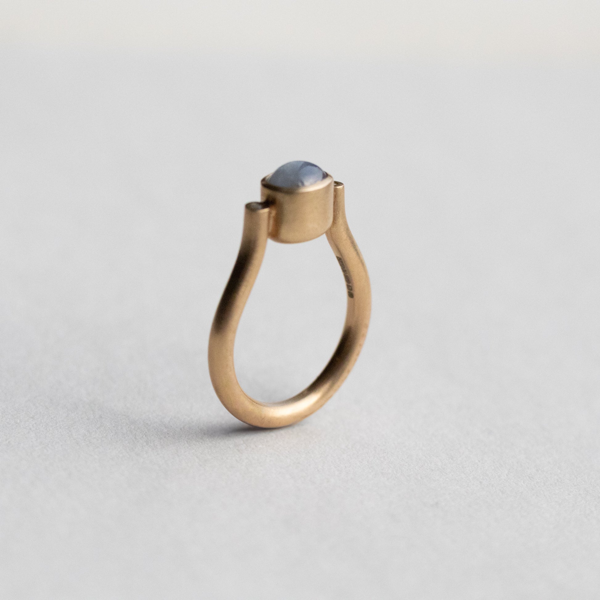 Modern 9ct yellow gold pillar ring with a single bezel-set grey cabochon star sapphire, photographed from a side view