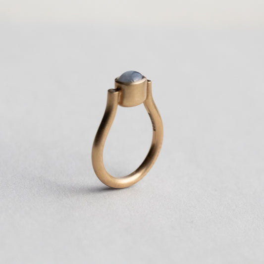 Modern 9ct yellow gold pillar ring with a single bezel-set grey cabochon star sapphire, photographed from a side view