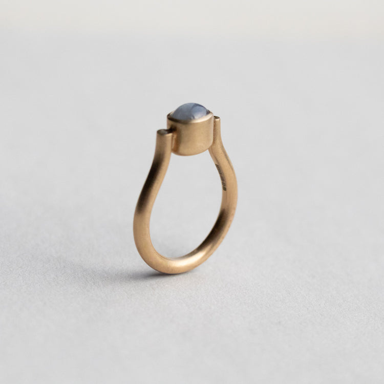 Modern 9ct yellow gold pillar ring with a single bezel-set grey cabochon star sapphire, photographed from a side view