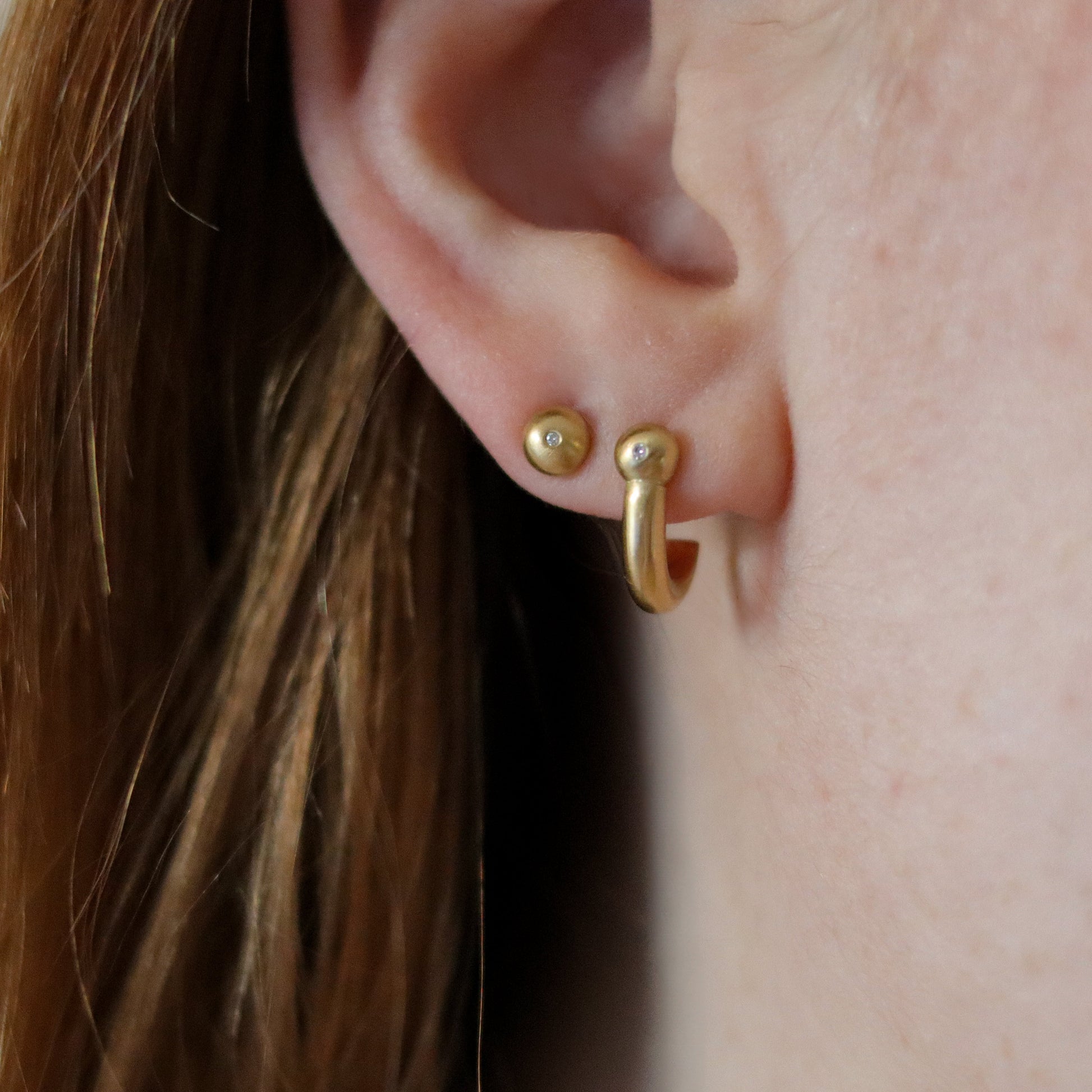 Close-up of ear wearing small solid 18ct gold diamond set hoop and stud earrings with a smooth, contemporary design.