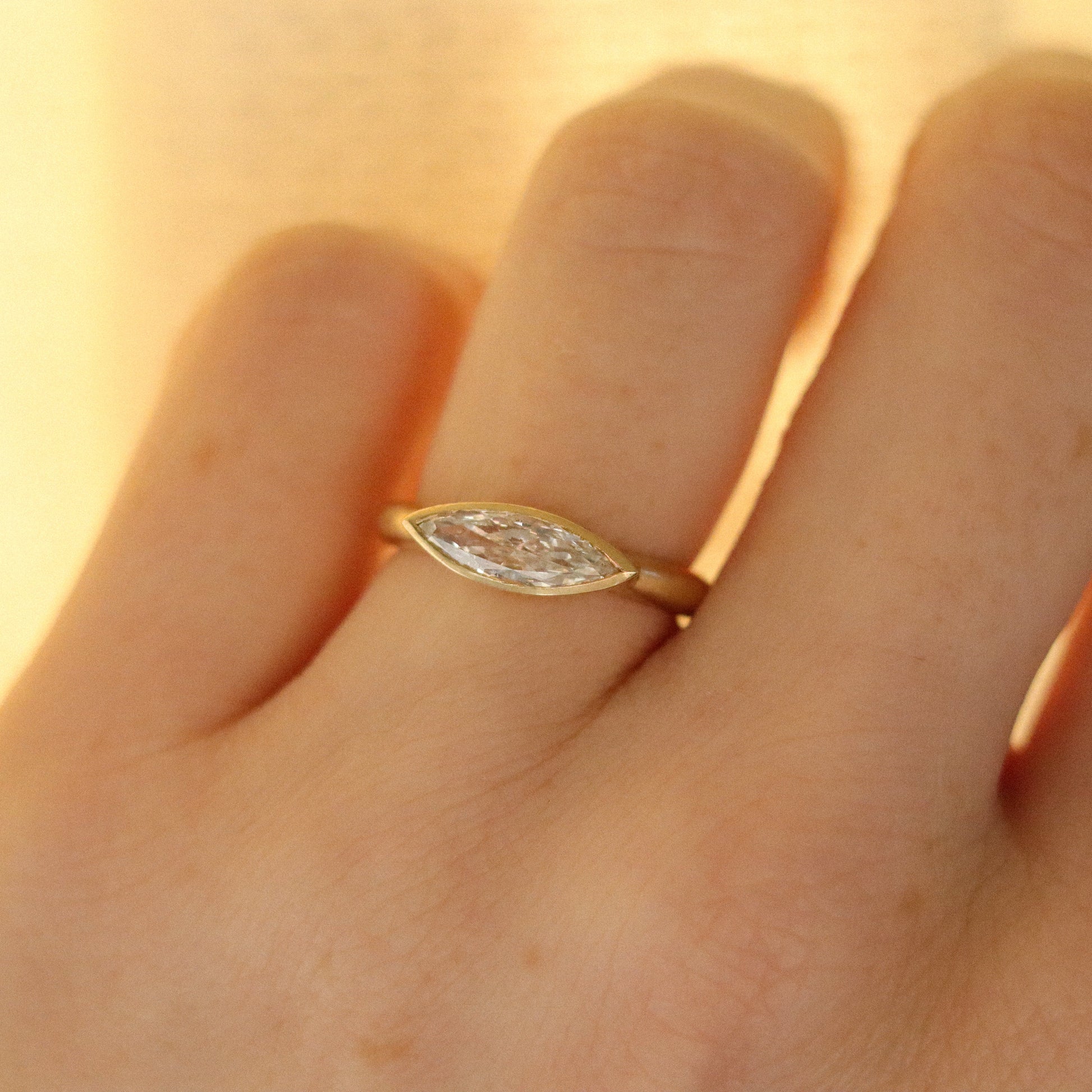 Elegant 18ct yellow gold ring set with a marquise-cut diamond in a minimalist bezel, worn on the finger
