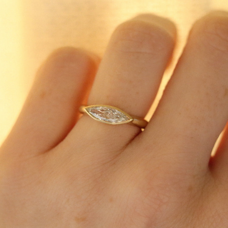 Elegant 18ct yellow gold ring set with a marquise-cut diamond in a minimalist bezel, worn on the finger