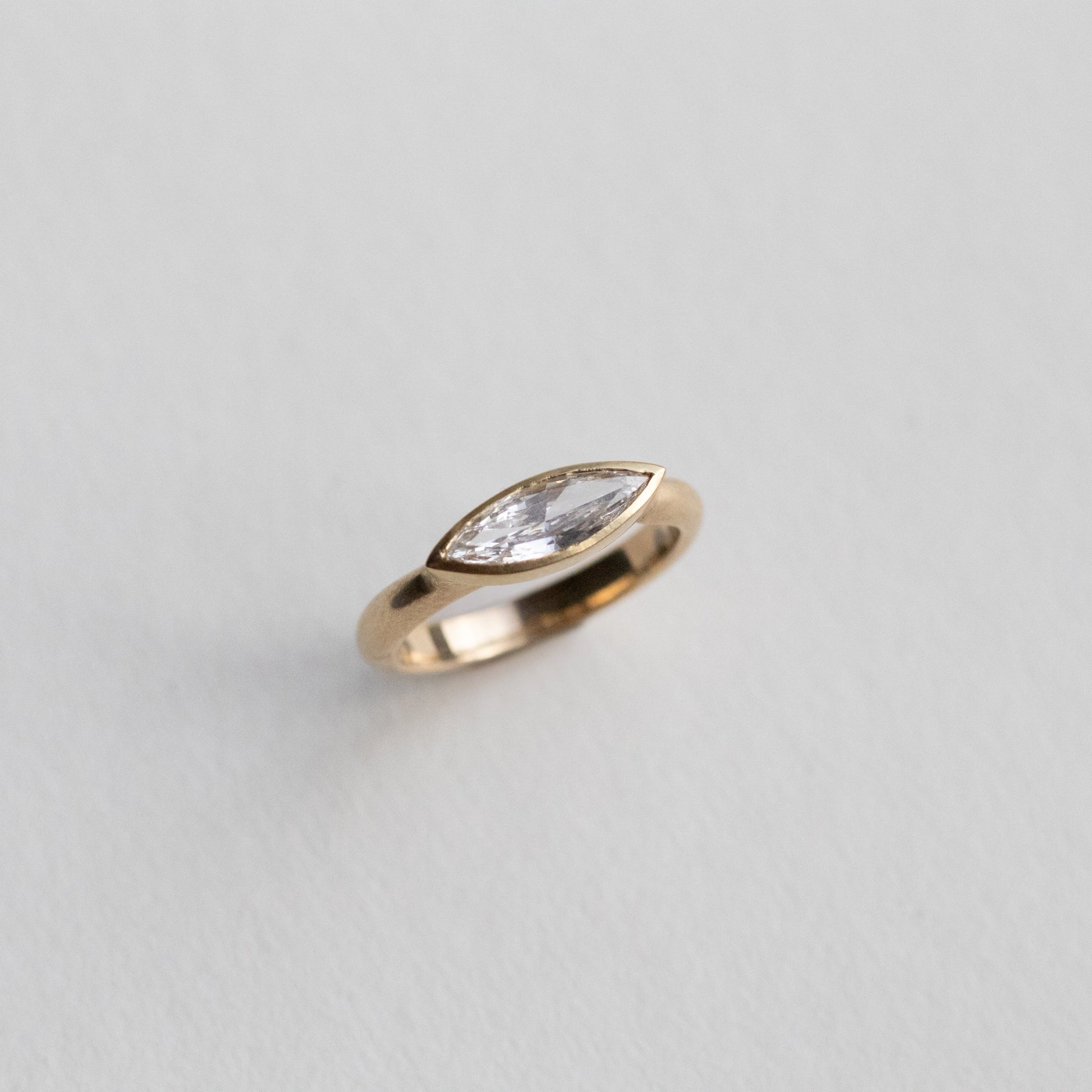 “Elegant 18ct yellow gold ring set with a marquise-cut diamond in a minimalist bezel, paper shot perspective view