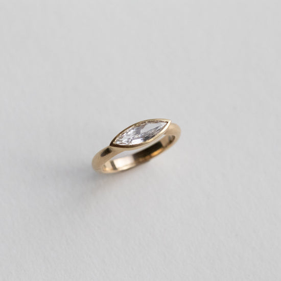 “Elegant 18ct yellow gold ring set with a marquise-cut diamond in a minimalist bezel, paper shot perspective view